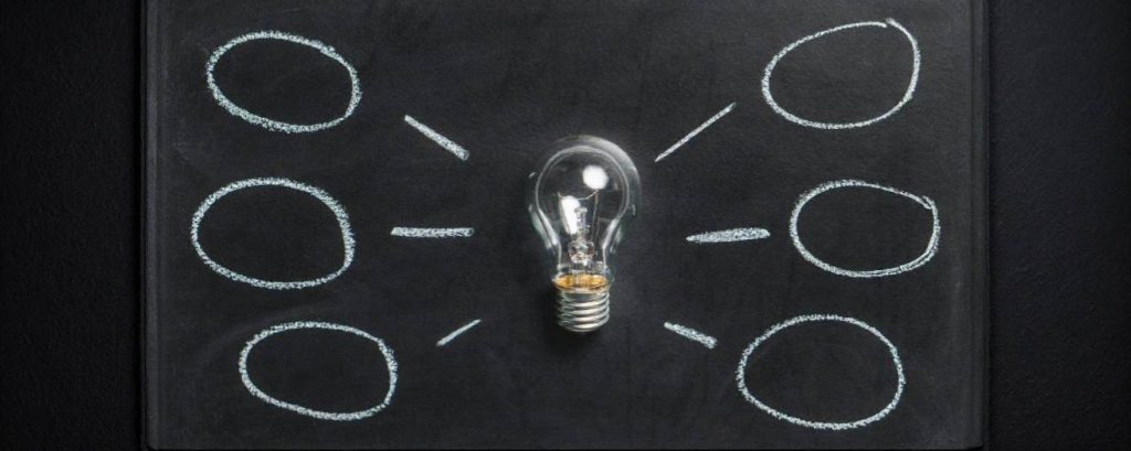 A light bulb placed on a blackboard with six empty chalk-drawn circles radiating outward, symbolising ideas or brainstorming concepts.